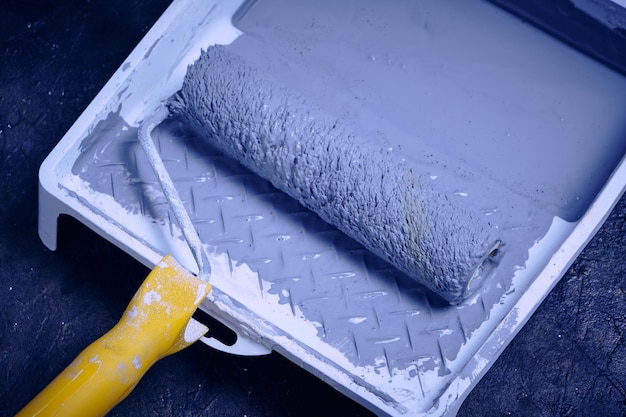 Rouleau à peinture avec poignée jaune dans le bac pour rouleau à peinture grise sur sol en béton