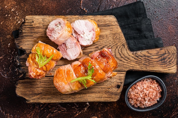 Rouleau de poulet rôti au fromage et aux herbes sur une planche de bois Fond sombre Vue de dessus