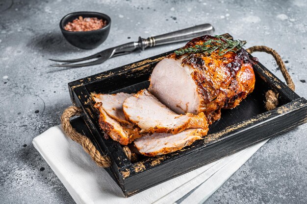 Rouleau de rôti de porc glacé dans un plateau en bois avec des herbes Fond gris Vue de dessus