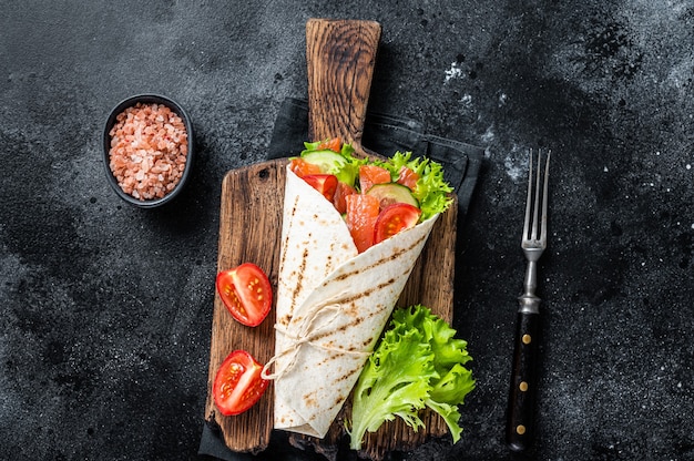 Rouleau de saumon tortilla Wrap avec salade, légumes. Table noire. Vue de dessus.