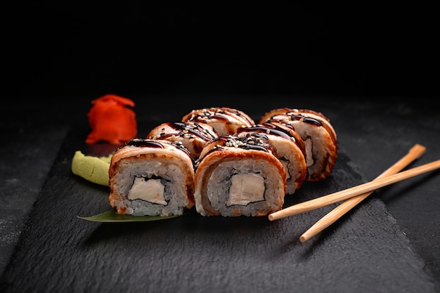 Rouleau de sushi à l'anguille et fromage à la crème, sur ardoise noire, sur fond noir