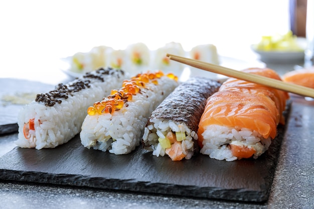 Rouleau de sushi au saumon, caviar rouge et caviar noir sur une plaque noire sur une surface en bois. Femme à l'aide d'un tapis roulant en bambou pour des sushis faits maison