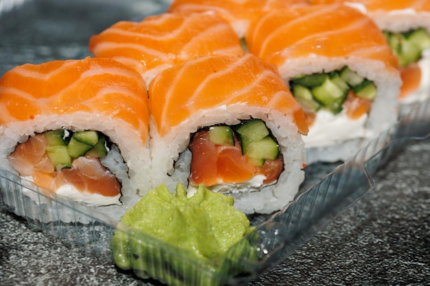 Photo rouleau de sushi avec du saumon, de l'avocat, du fromage à la crème d'anguille fumée sur un fond noir, nourriture japonaise