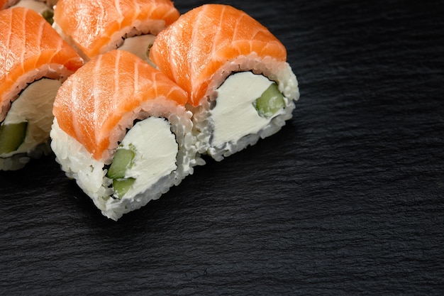 Rouleau de sushi de Philadelphie avec concombre de saumon et fromage à la crème sur fond noir pour le menu Cuisine japonaise