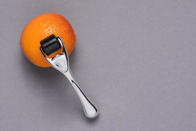 Rouleau de visage de beauté sur une orange sur fond gris foncé