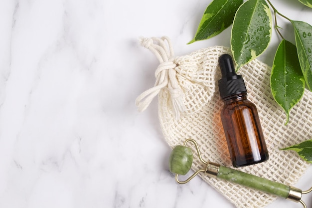 Rouleau de visage de bouteille de sérum sans marque avec des feuilles sur fond de marbre Rouleau de visage de jade pour la thérapie de massage facial Traitement anti-âge et tonifiant