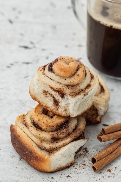 Rouleaux de cannelle et un café américain dans une tasse en verre sur une vieille table en bois blanc.