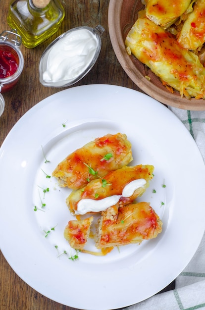 Rouleaux de chou maison avec carottes, sauce tomate rouge et crème sur une plaque blanche