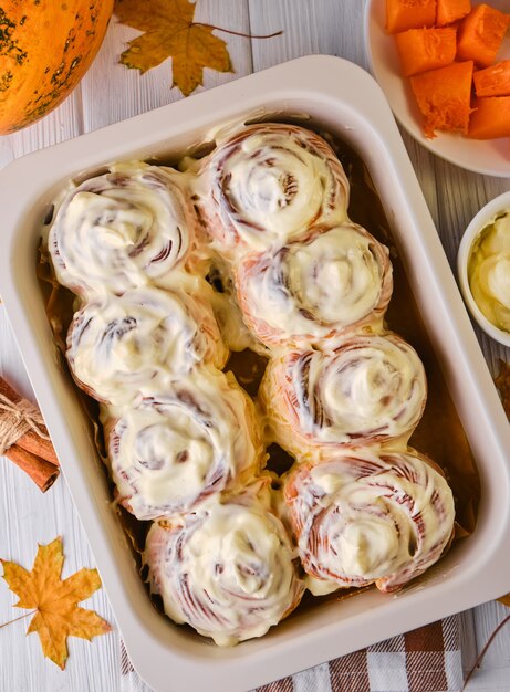 Rouleaux de citrouille à la cannelle faits maison avec du fromage à la crème dans un plat allant au four, à plat, vue de dessus. Pâtisserie maison d'automne de saison - cannelle pour le petit déjeuner ou les vacances.