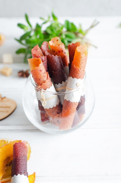 Rouleaux de cuir de fruits faits maison dans un bol en verre sur table en bois blanc, pastille de bonbons