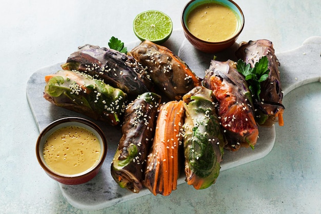 Rouleaux d'été arc-en-ciel végétaliens dans une enveloppe de riz avec une sauce aux amandes épicée des aliments sains