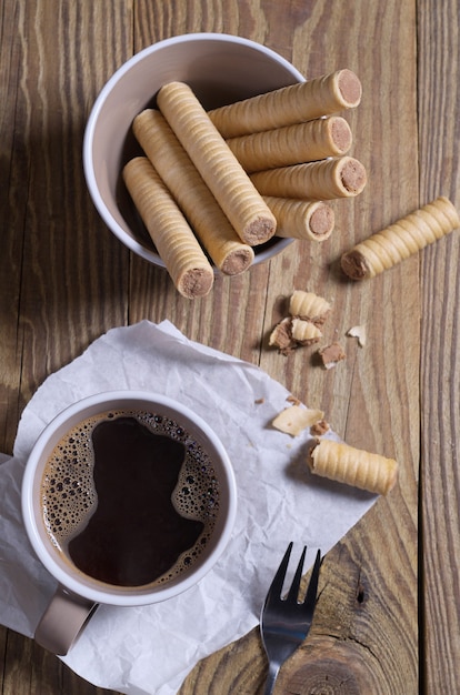 Rouleaux de gaufres au chocolat dans un bol et une tasse de café sur une table en bois, vue de dessus