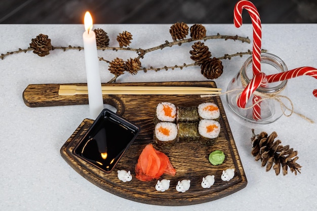 Rouleaux japonais avec du poisson rouge sur une planche à découper en bois Décoration de table avec des bougies et des bonbons Concept de Noël