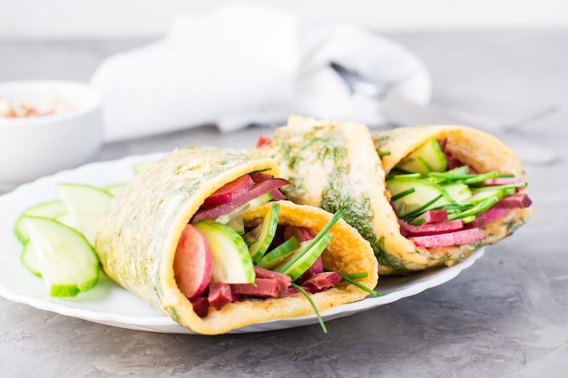 Rouleaux d'oeufs remplis de pastrami, de concombre, de radis et d'oignons verts sur une assiette sur la table.