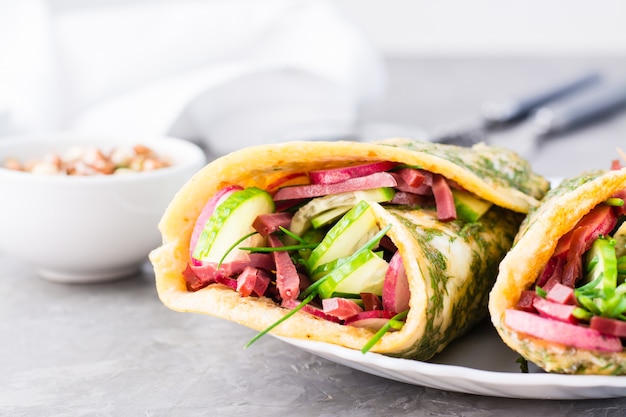 Rouleaux d'oeufs remplis de pastrami, de légumes et d'oignons verts sur une assiette sur la table.