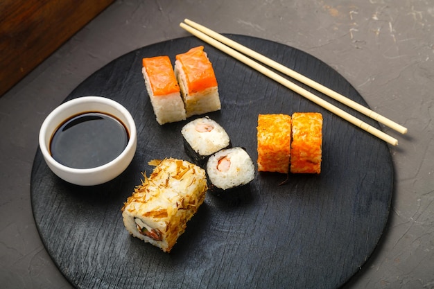 Rouleaux de poisson et de crevettes sur une planche ronde à côté de bâtonnets de sauce soja sur fond sombre