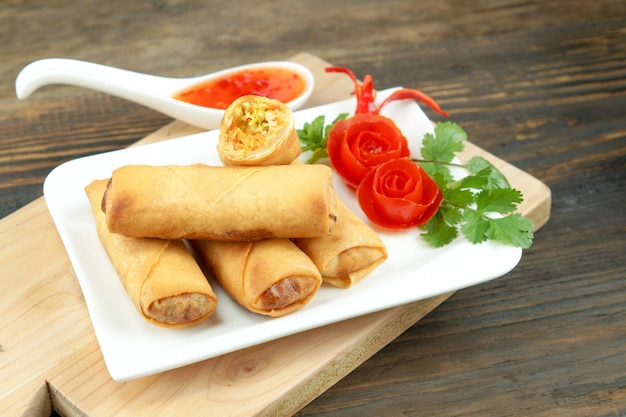 Photo rouleaux de printemps chinois frits servis avec une sauce chili et décorés de tomates roses à feuilles vertes sur bois, espace. concept de cuisine asiatique