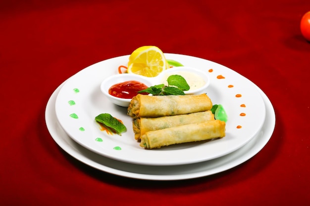 Des rouleaux de printemps croustillants avec des sauces de trempage servis dans une assiette isolée sur un fond rouge vue latérale rapprochée de la nourriture arabe