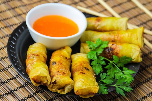 Rouleaux de printemps avec sauce sucrée sur plaque noire