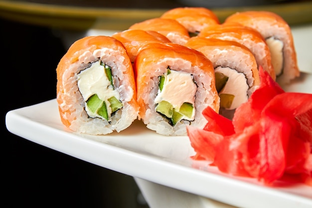 Rouleaux de saumon et concombre, fromage et wasabi sur une plaque blanche