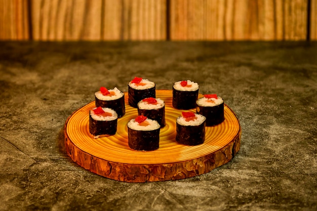 Rouleaux de sushi appétissants avec du riz au saumon et du poivron rouge sur une assiette en bois