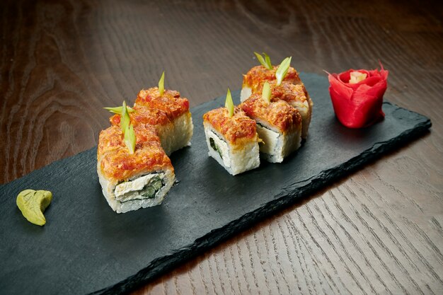 Rouleaux de sushi au concombre, au fromage de Philadelphie et à l'anguille sur une ardoise noire sur une table en bois. Cuisine japonaise.