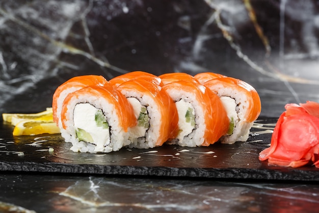 Rouleaux de sushi au concombre, avocat, saumon et fromage à la crème à l'intérieur sur l'ardoise noire isolé sur fond de marbre noir. Philadelphia roll sushi. Menu de sushi. Photo horizontale.