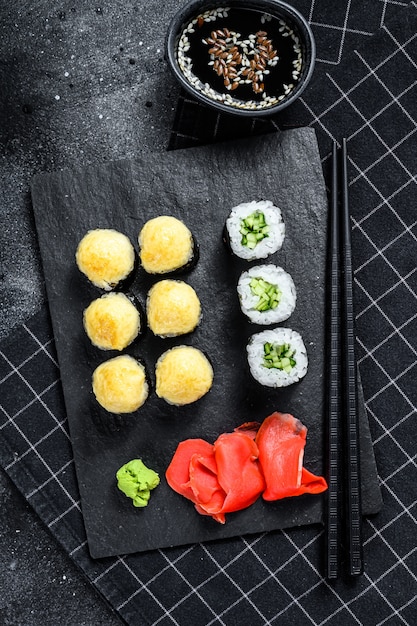Rouleaux de sushi au concombre, saumon et crevettes sur un plateau en pierre. Fond noir. Vue de dessus