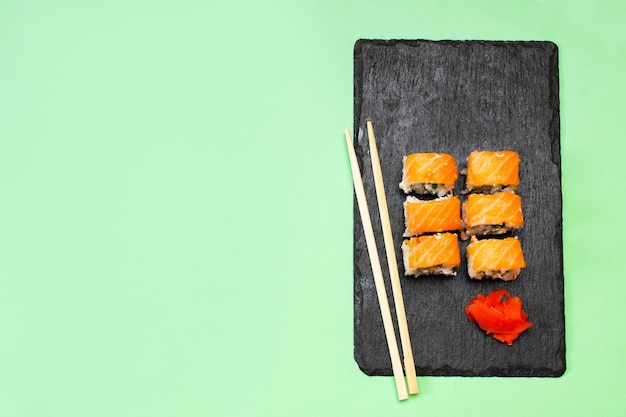 Rouleaux de sushi au poisson avec du saumon, du wasabi et des baguettes sur une planche à découper noire sur vert. Fruit de mer