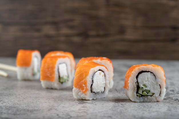 Rouleaux de sushi au saumon, anguille fumée, avocat, fromage à la crème et baguettes jetables en bois.