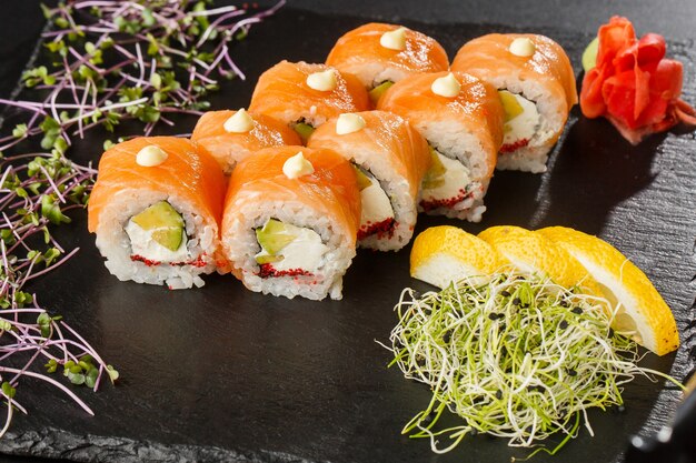 Rouleaux de sushi au saumon, avocat, caviar de poisson volant et fromage à la crème à l'intérieur sur fond noir