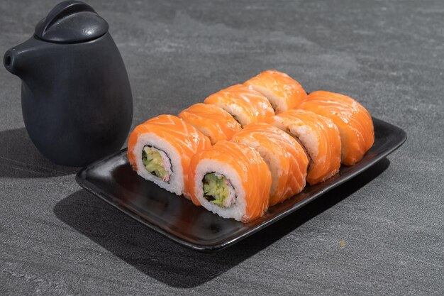 Rouleaux de sushi au saumon, avocat et concombre sur une plaque rectangulaire noire sur fond d'ardoise noire