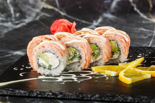 Rouleaux de sushi au saumon flammé, concombre et fromage à la crème à l'intérieur sur une ardoise noire isolée sur fond de marbre noir. Philadelphia roll sushi au concombre. Menu de sushi. Photo horizontale.