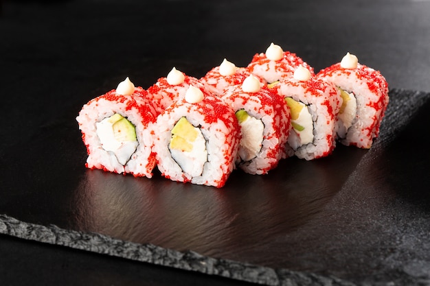 Rouleaux de sushi avec avocat, crevettes et fromage à la crème à l'intérieur sur fond noir