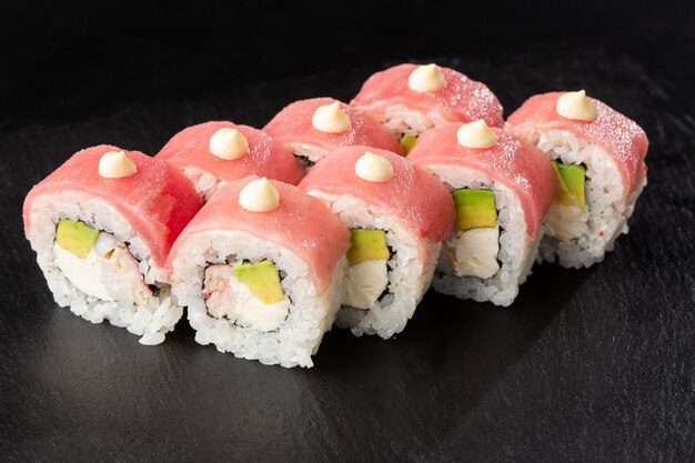 Rouleaux de sushi avec avocat, thon, crevettes, chair de crabe et fromage à la crème à l'intérieur sur ardoise noire