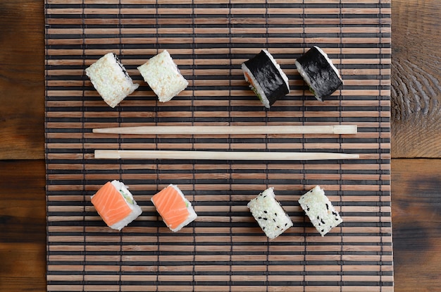 Des rouleaux de sushi et des baguettes en bois se trouvent sur un tapis de serwing en paille de bambou.