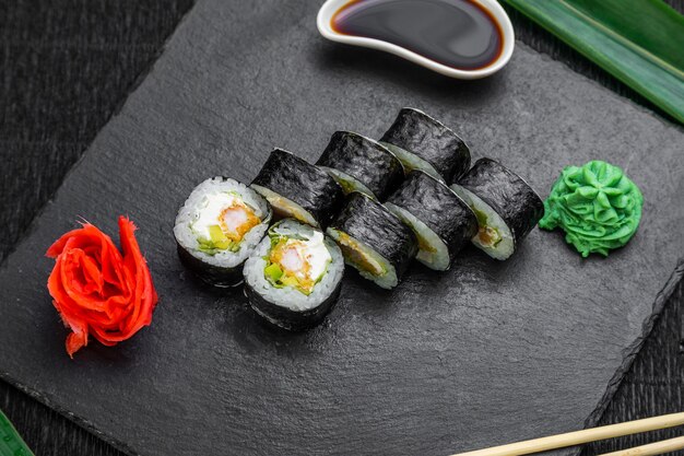 Rouleaux de sushi disposés sur un fond sombre décoré de feuilles de bambou et de baguettes