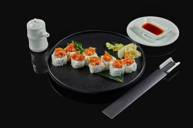 Rouleaux de sushi épicés avec du riz, des normes, de la mayonnaise, du caviar de tobiko et du saumon sur une plaque en céramique noire sur une surface noire. Cuisine traditionnelle japonaise.