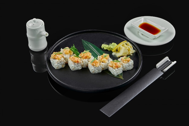 Rouleaux de sushi épicés avec du riz, des normes, de la mayonnaise, du caviar de tobiko et des pétoncles sur une plaque en céramique noire sur une surface noire. Cuisine traditionnelle japonaise.