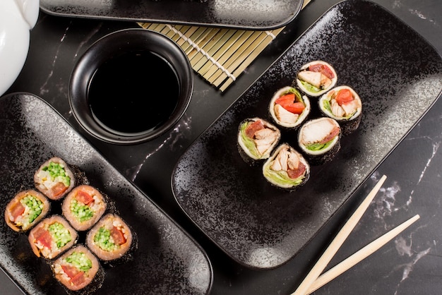 Rouleaux de sushi frais et savoureux avec bâtons et sauce sur fond noir