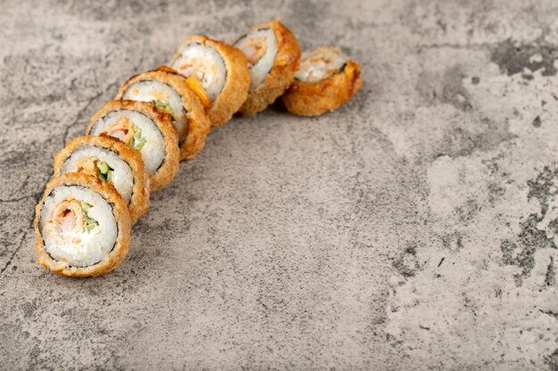 Rouleaux de sushi frits chauds avec du saumon, de l'avocat et du fromage placés sur une table en pierre.