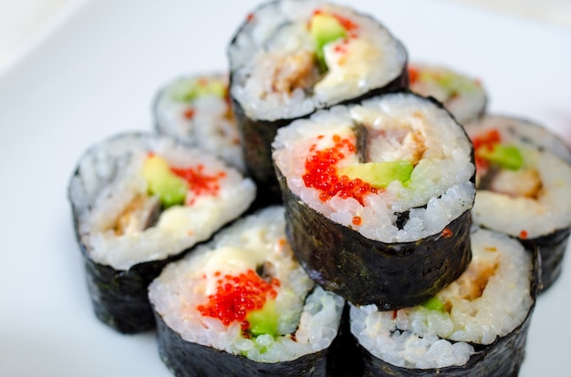 Rouleaux, sushi et gingembre sur une assiette blanche et une surface légère.