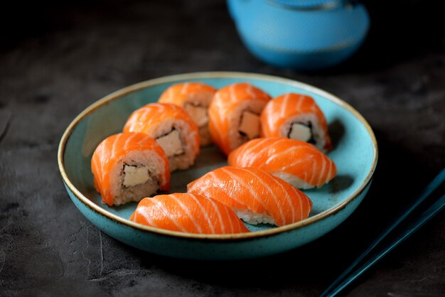 Rouleaux De Sushi Maison Philadelphia Et Nigiri Dans Une Assiette Bleue Sur Une Surface Noire.