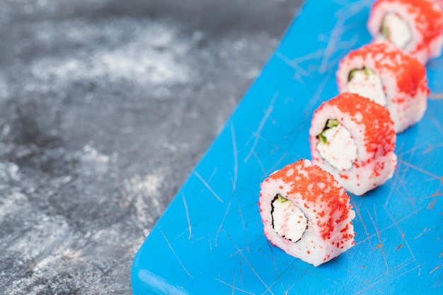 Rouleaux de sushi de Philadelphie avec du fromage à la crème frais placé sur une planche de bois bleue.