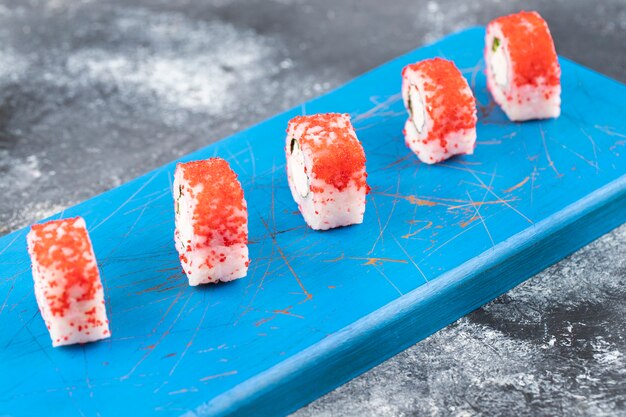 Rouleaux de sushi de Philadelphie avec du fromage à la crème frais placé sur une planche de bois bleue.