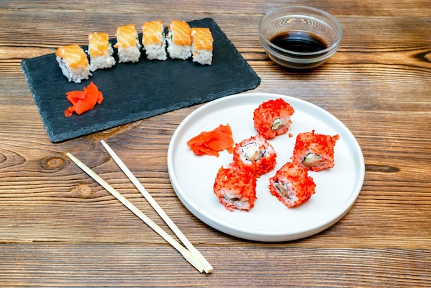 Rouleaux de sushi de poisson avec caviar rouge saumon et baguettes sur une assiette de service en céramique grise sur fond rustique en bois gros plan Service de restauration de fruits de mer du concept de restaurant