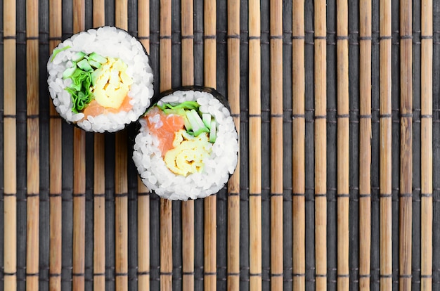 Des rouleaux de sushi reposent sur un tapis de serwing en paille de bambou