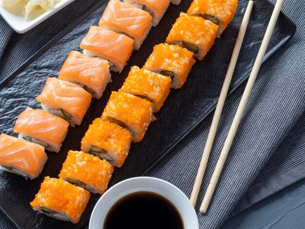 Roulez Philadelphie et la Californie sur une plaque noire. Vue de dessus, mise à plat. gingembre, wasabi et sauce soja à proximité. cuisine japonaise traditionnelle