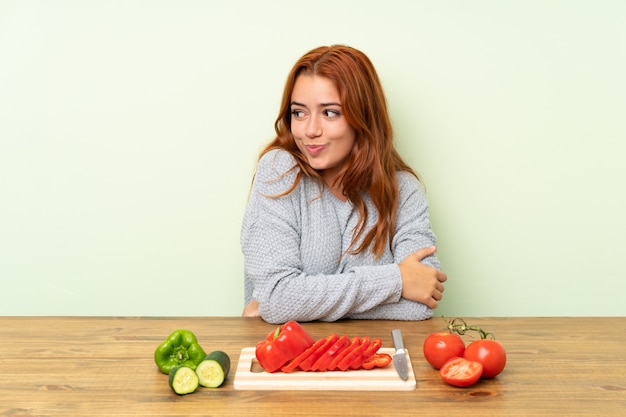 Rousse adolescente avec des légumes dans une table en pensant à une idée