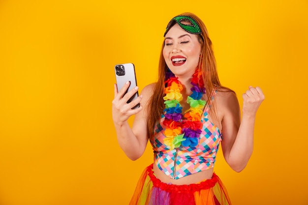 Rousse brésilienne en tenue de carnaval avec un collier de fleurs autour du cou montrant un smartphone